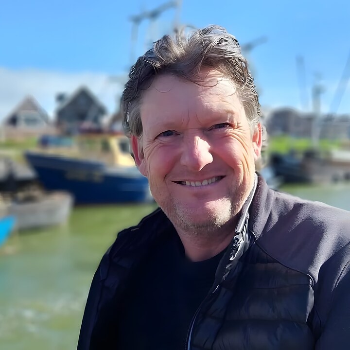 Hans van Schaick in de haven van Makkum, met vissersboten en Friese gevels achter zich