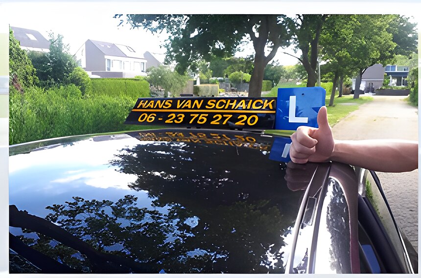 De lesauto van Hans van Schaick op een dorpsweg, met een leerling die het L-bordje omhoog houdt